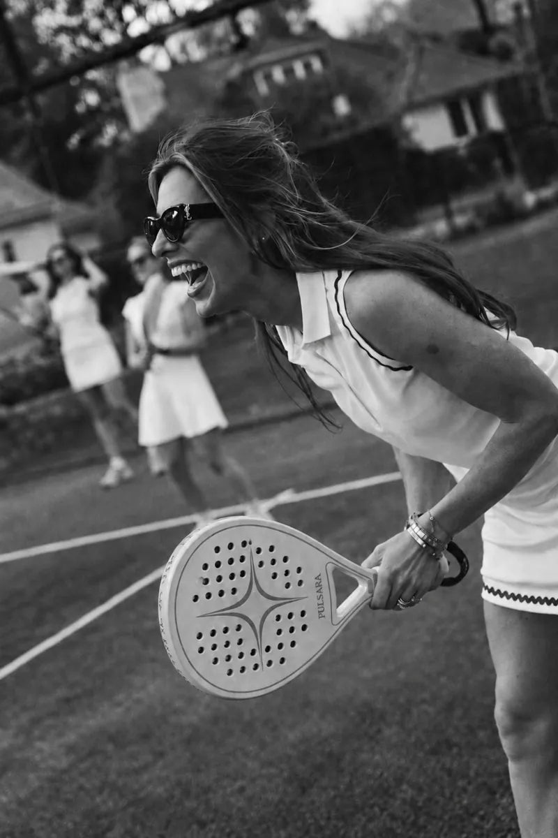 A woman laughing on court with her Pulsara racket, friends behind her